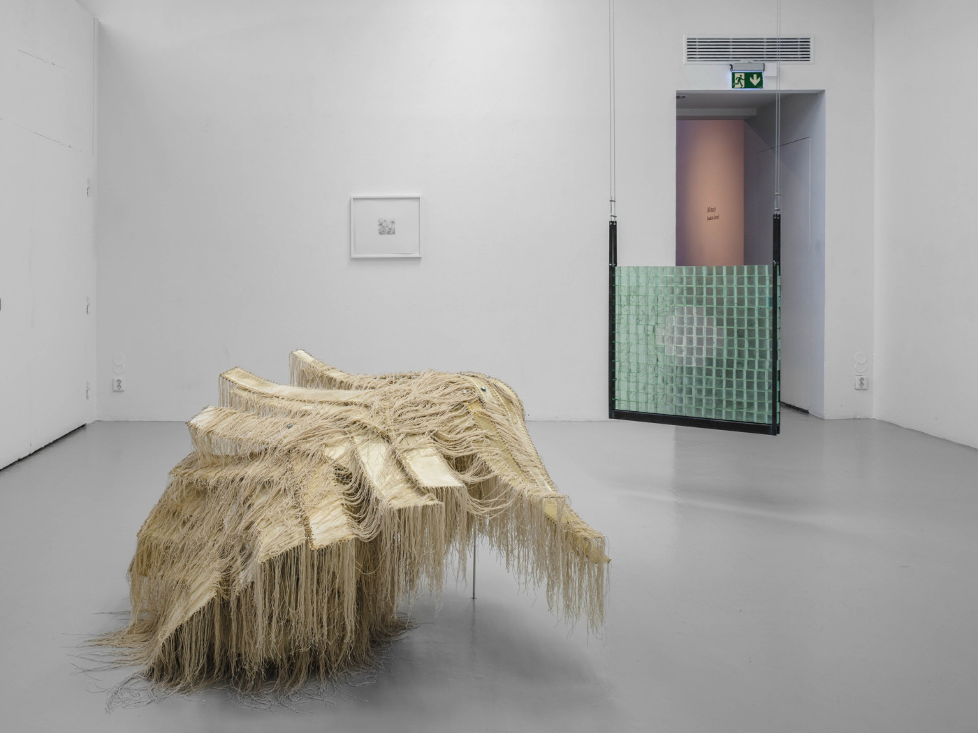 Fringed sculpture on the floor, a green grid panel behind